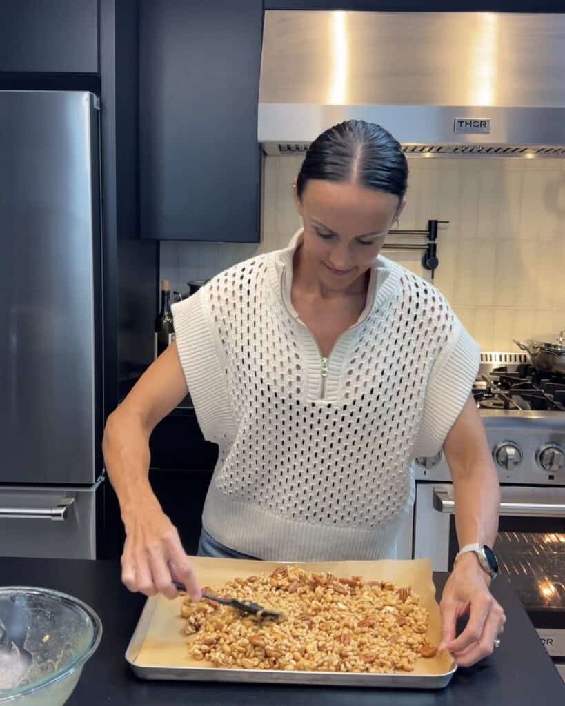 Caitlin preparing homemade peanut butter trail mix with maple, toasted nuts, crispy rice cereal, and Redmond Real Salt on a sheet pan in a home kitchen.
