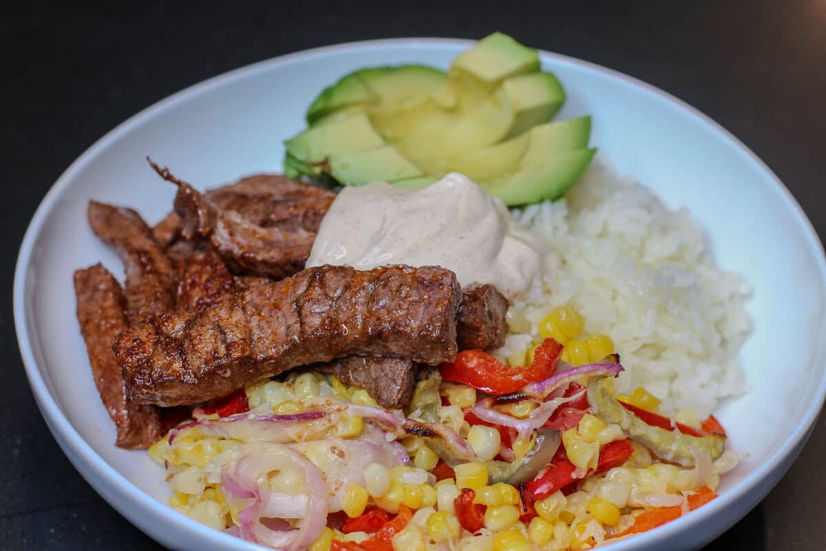 Sheet pan chili lime beef taco bowl with rice, roasted peppers and corn, avocado, and chili lime sour cream.