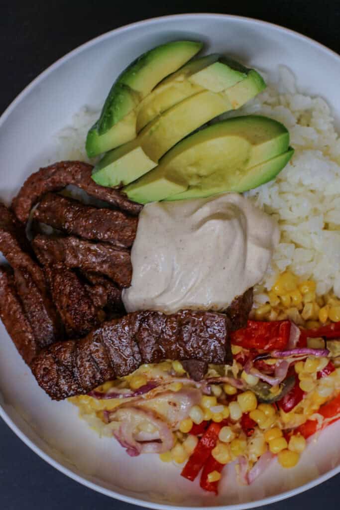 Close-up of a chili lime beef taco bowl with jasmine rice, avocado, roasted vegetables, melted cheese, and sour cream.