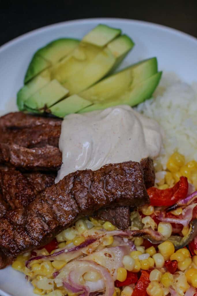 Chili lime beef taco bowl topped with avocado and creamy chili lime sour cream, served with rice and roasted vegetables.